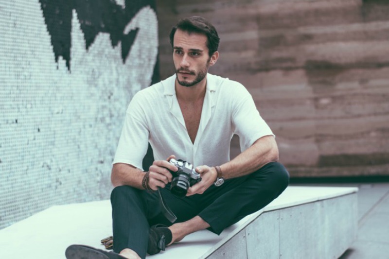 Young handsome photographer sitting and holding a camera i his hands, outdoors in the city,